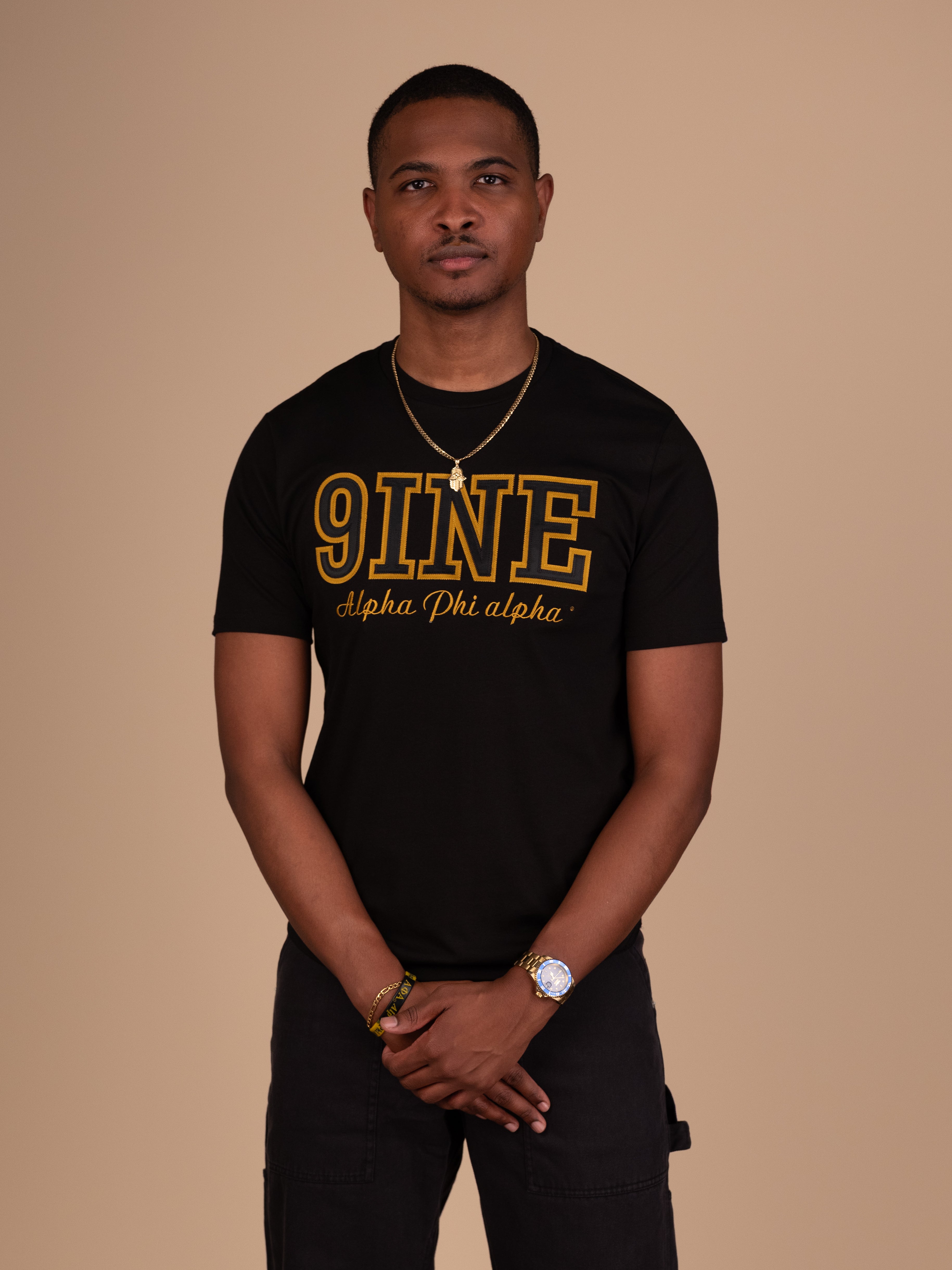 Man wearing a black t-shirt with '9INE' logo on a beige background